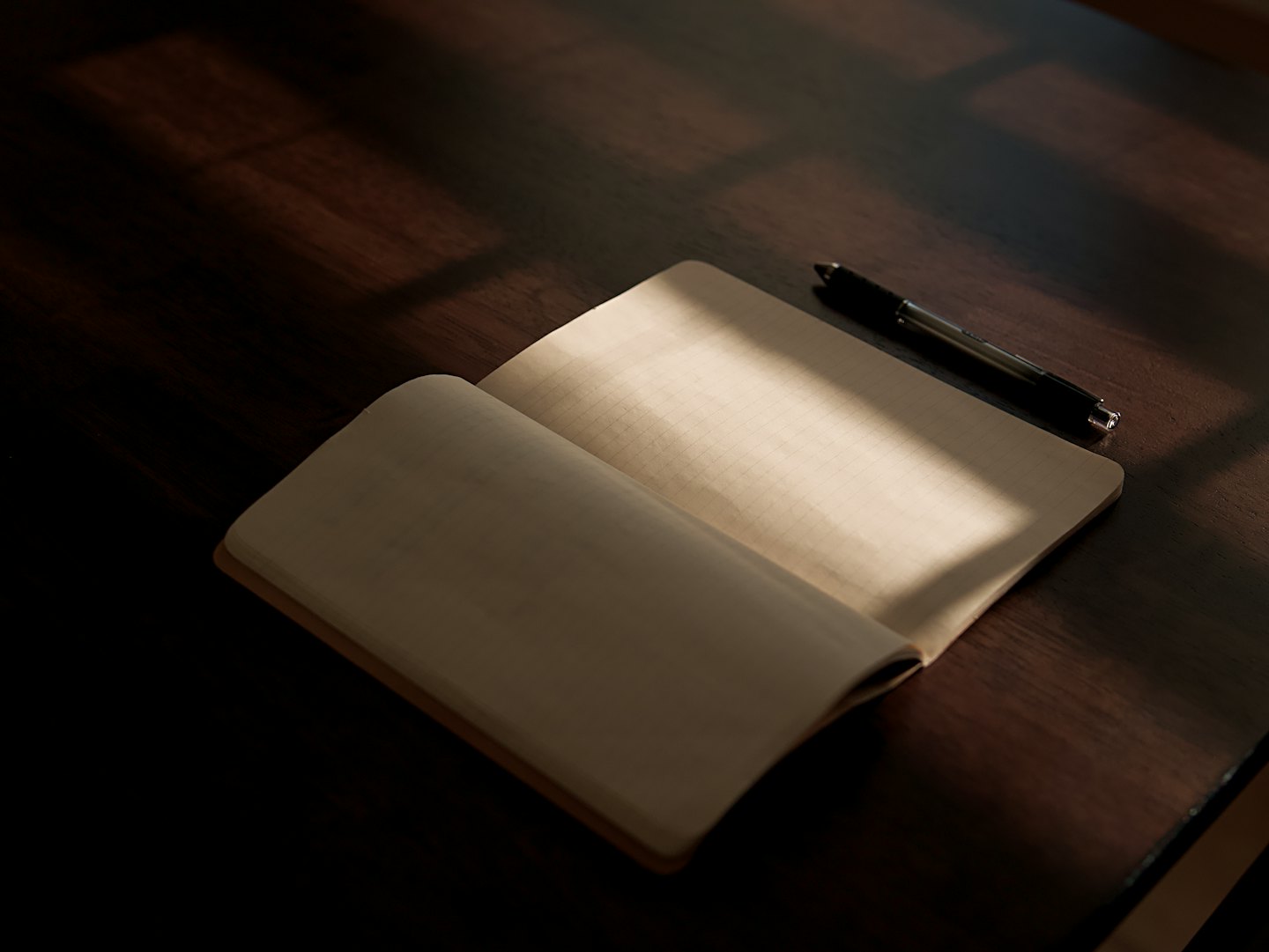 Un taccuino aperto e una penna su una scrivania di legno.