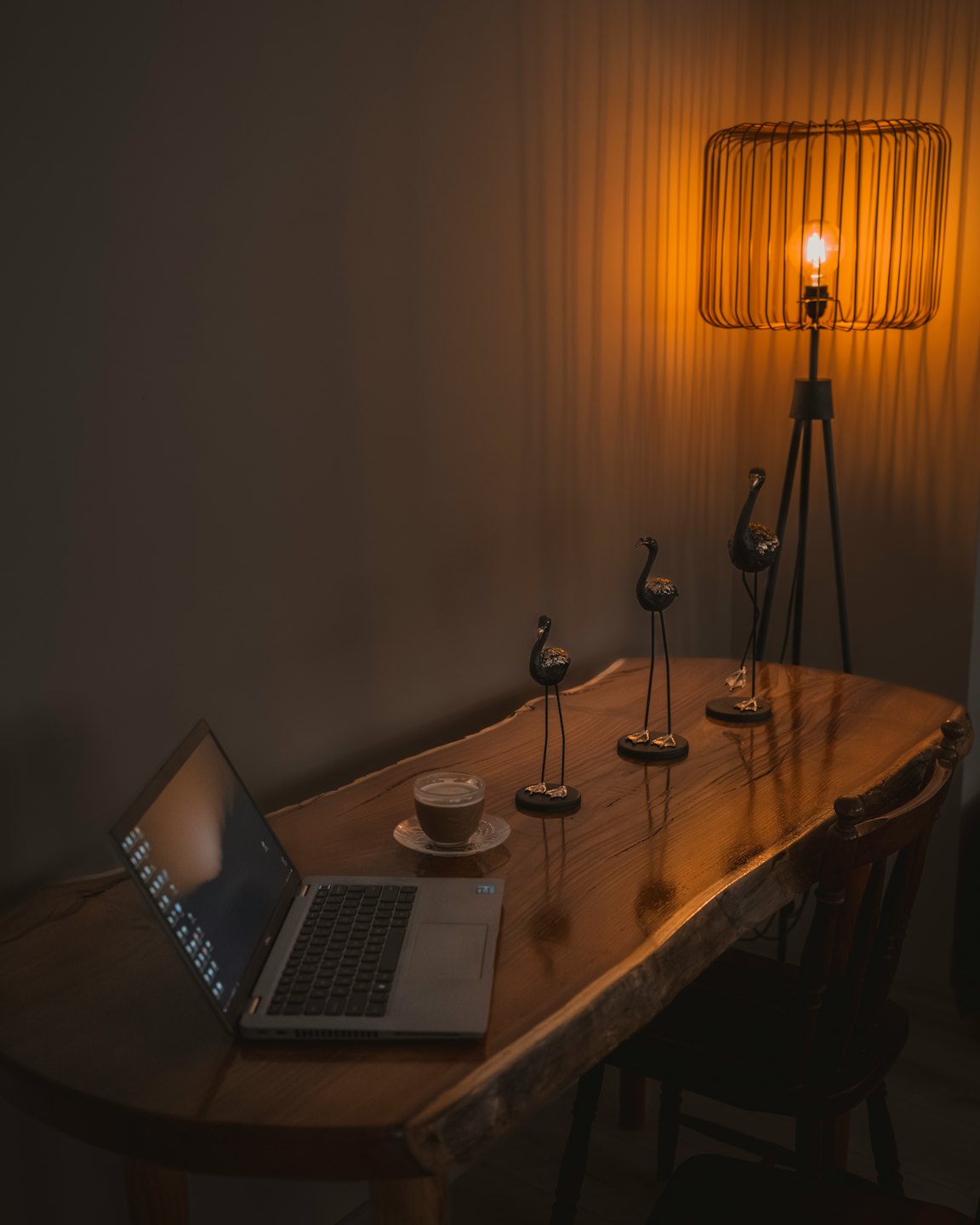 Computer portatile e caffè su una scrivania di legno con statuette di uccelli.